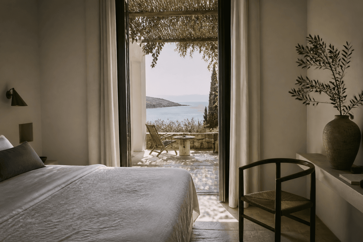 A quiet boutique hotel room opening onto a shaded terrace and distant sea
